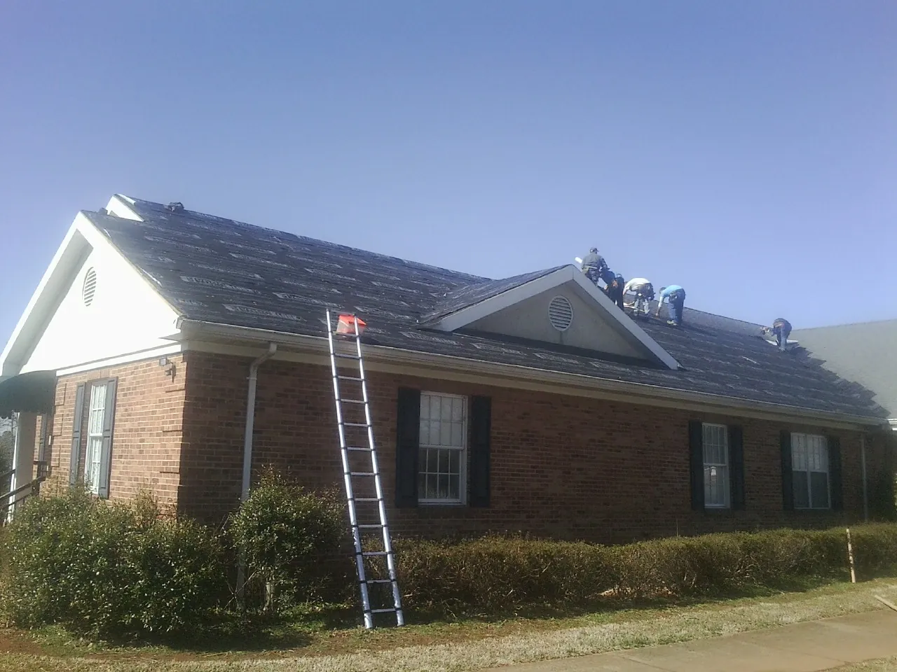 Crew tearing shingles off a brick ranch roof with a ladder set — Metal Roof Repair work by our crew in Red Banks