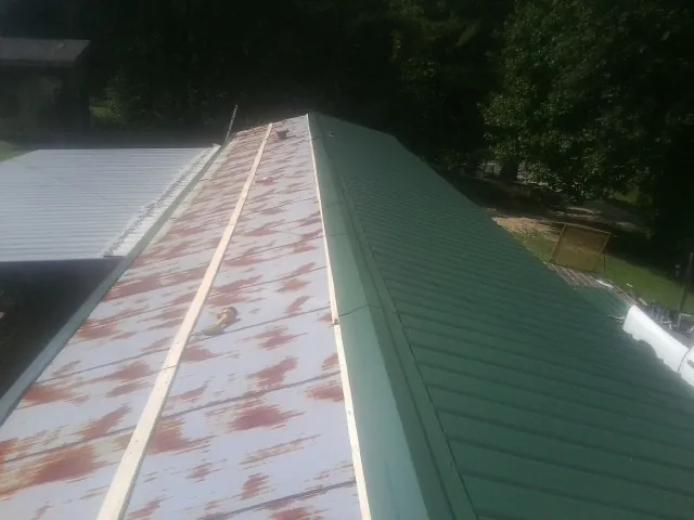 Old rusted panels beside newly installed green metal roofing — Wind Damage Roof Repair by Roofing Brothers in Red Banks