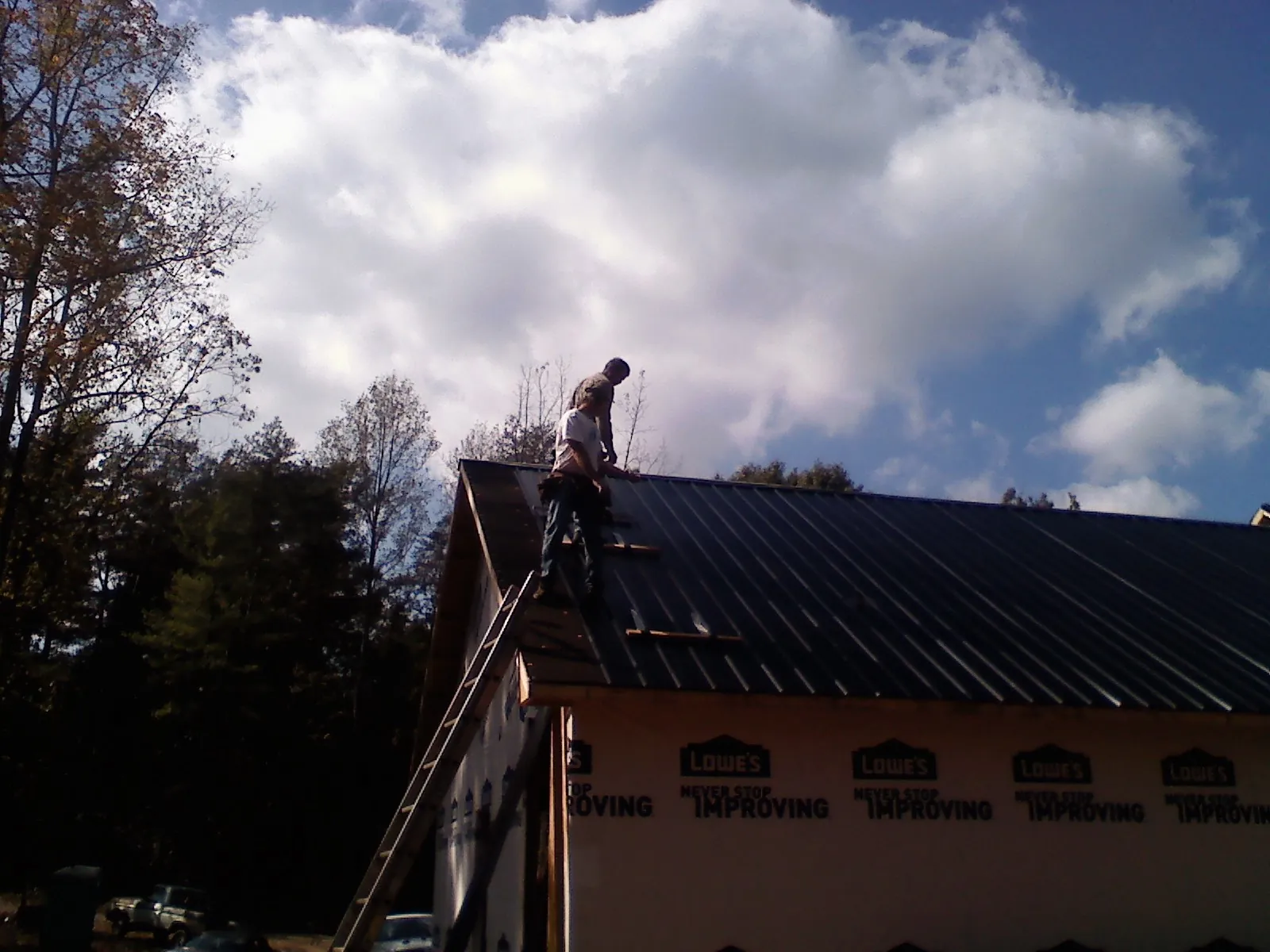 Roofer fastening dark metal panels high against a cloudy sky, from a Roof Inspection job in Red Banks