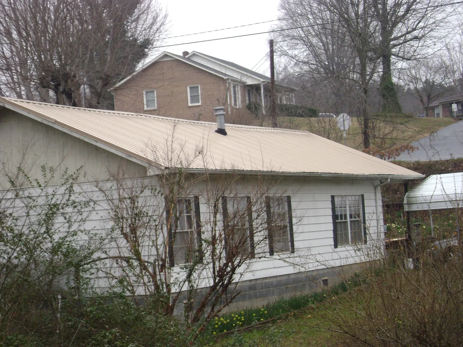 Tan metal roof on a white sided house set into a hillside in Red Banks