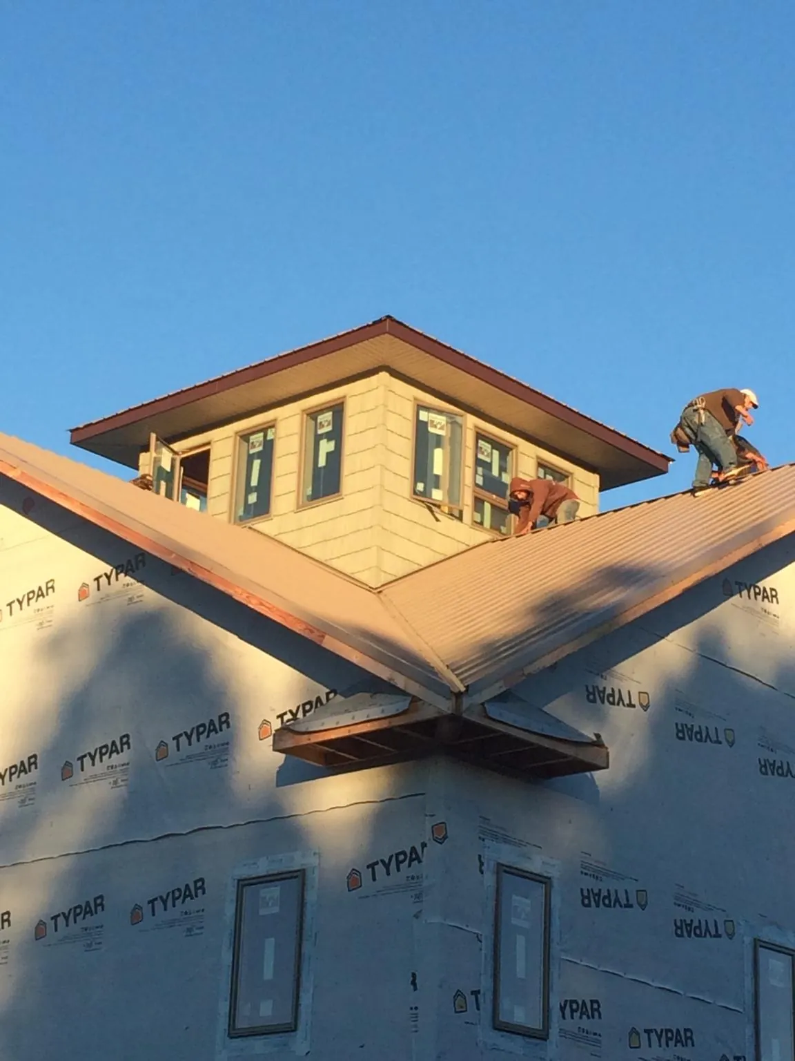 Roofers working around a rooftop cupola on a new metal roof at sunset — Roof Waterproofing in Red Banks by Roofing Brothers